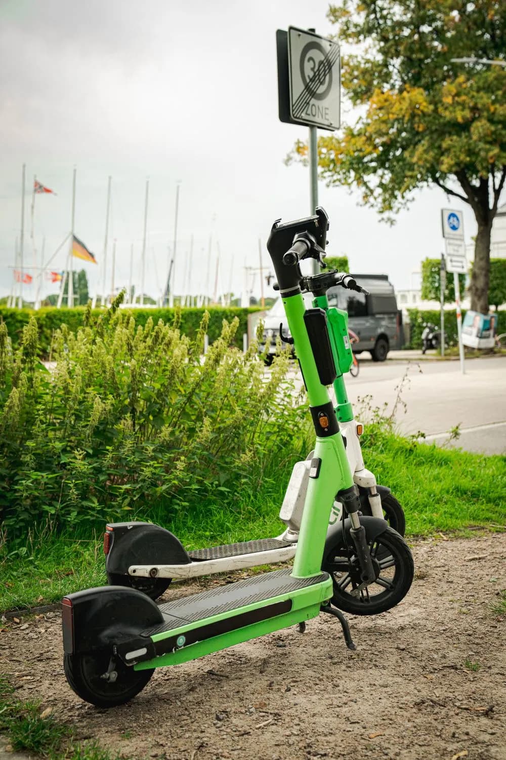 Dos patinetas eléctricas verdes estacionadas junto a un jardín